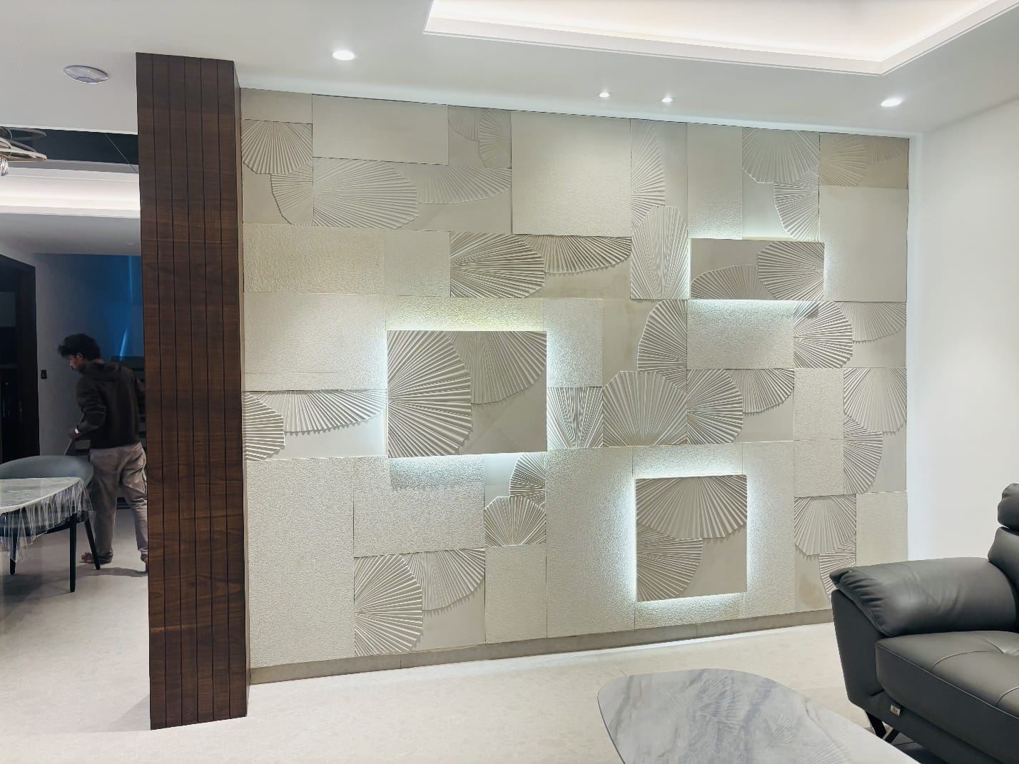 Open-plan luxury interior showing dining table and chairs beside living lounge, united by a carved stone feature wall