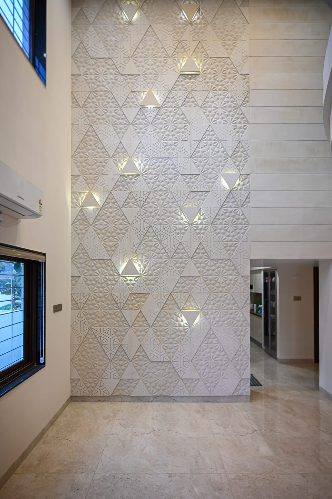 Soaring vertical living room stone elevation with 3D faceted geometric marble panels and cove lighting