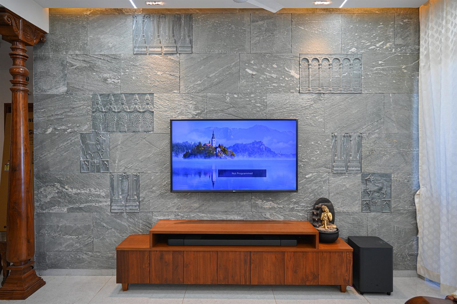Mounted wide-screen TV on textured grey stone slab wall with low-profile wooden media console